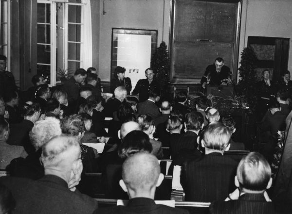 Heinrich Hollands of the "Aachener Nachrichten" speaking to a conference of German journalists at Marburg University following World War II.  To Hollands' right is newspaperman James Aronson, the American press officer.