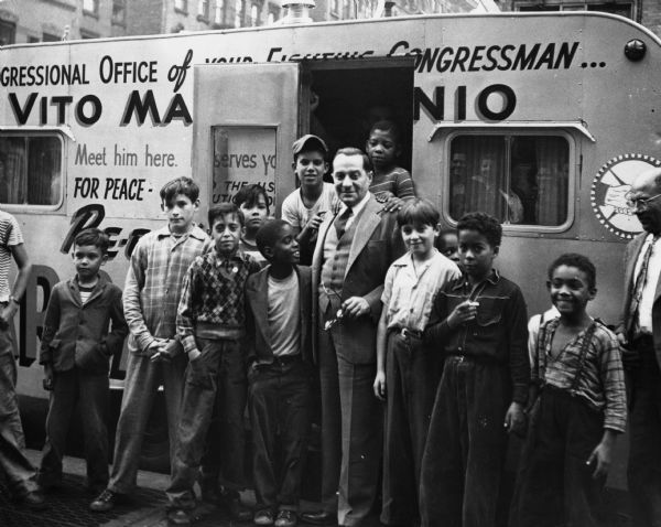 Vito Marcantonio, New York congressman, with some future voters. He is standing outdoors with a group of young boys in front of his office, which is in a trailer.