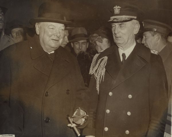 Admiral William D. Leahy, the personal representative of President Truman, greets former Prime Minister Winston Churchill at the Washington D.C. airport. Leahy was raised in Ashland, Wisconsin. UPI reporter, Merriman Smith, who donated this image to the Archives, is visible between the two men.