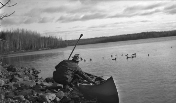 A duck hunter at the edge of a rocky shoreline, probably Sigurd Olson.