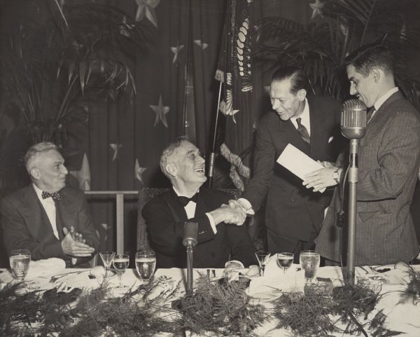 At the annual dinner of the White House Correspondents Association, President Franklin Roosevelt congratulates Raymond Brandt, the winner of the Clapper Award. On the left is Merriman Smith, president of the association and "dean of the White House correspondents." When Roosevelt died at Warm Springs, Georgia, less than a month later, Smith was there too.