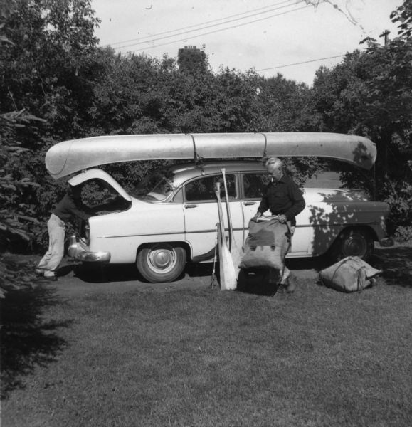 Sigurd Olson and another man stowing camping gear into an automobile for a canoe trip.
