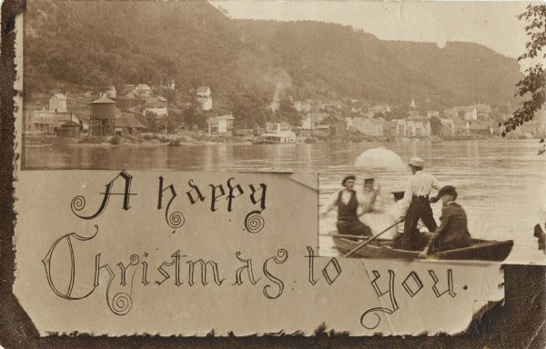 Christmas postcard of four men and one woman in a rowboat on the Mississippi River. In the background is the town of Alma at the foot of bluffs. The woman is holding an umbrella."A happy Christmas to you" is at the bottom of the postcard.