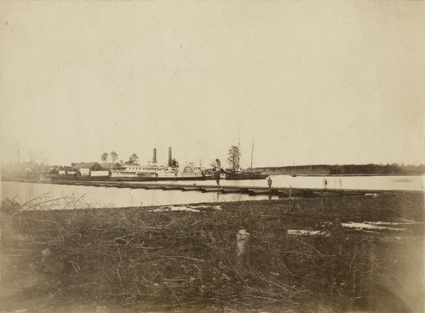 View from shoreline of the side-wheel steamship "Thomas Powell," probably in southern waters. Industrial buildings are in the background.