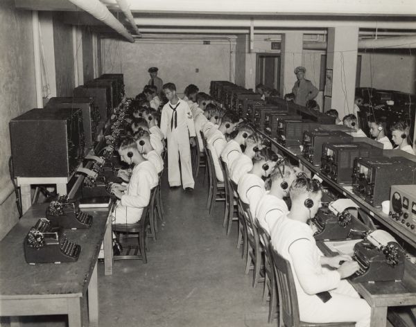 A Navy student oversees other students in a typing class at the U.S. Naval Training School (Radio).