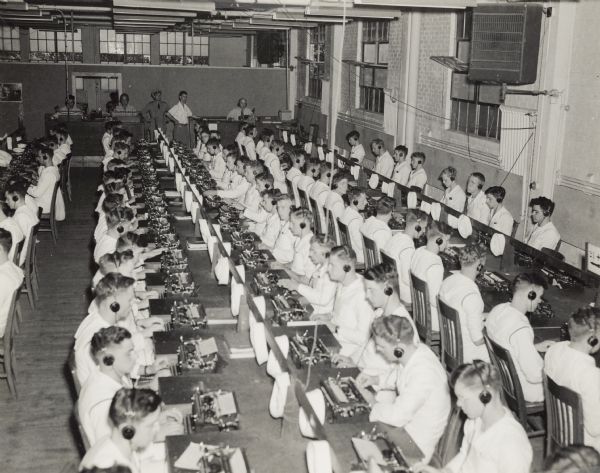 Elevated view of a classroom of Naval students wearing headphones while learning how to type at the U.S. Naval Training School (Radio).