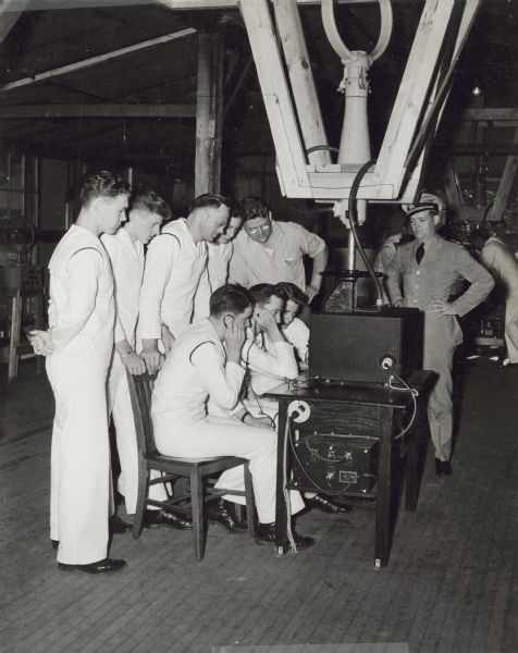 Naval students operate a radio while an officer looks on at the U.S. Naval Training School (Radio).