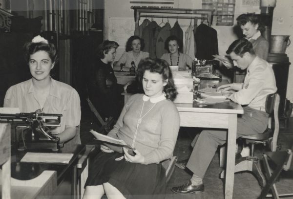 Six women and one man take messages at the Truax Field Message Center, during World War II. Beatrice Lamoreux is sitting at the back table on the left side. She, and her husband Leon, taught typing and telegraphy to Naval students at the U.S. Naval Training School (Radio).