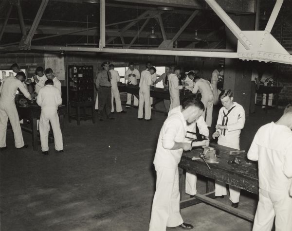 A group of Naval students learn to use hacksaws in a machine shop at the U.S. Naval Training School (Radio).