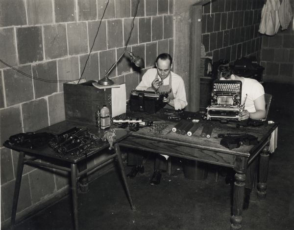 Two men are repairing typewriters at a table at the U.S. Naval Training School (Radio).