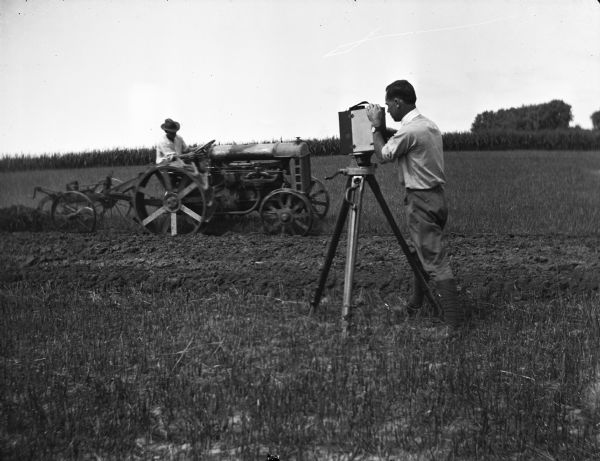 A photographer is taking a photograph of another man plowing a field with a tractor. The tractor is probably a Fordson and the implement dealer was probably Louis F. Schoelkopf, one of the first authorized Ford dealers in Madison. The dealership was open from 1905-1924 and was located at 210-214 East Washington Avenue. There was also a branch office in Mazomanie, Wisconsin. Schoelkopf was the first president of the Madison Automobile Dealers Association.
