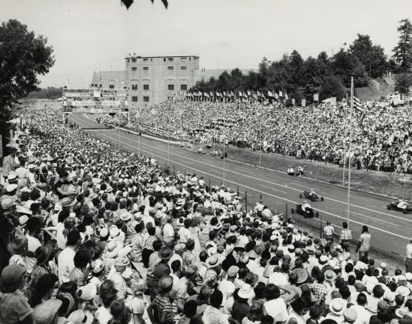 Elevated view of spectators in the grandstands at Derby Downs watching three racers participate in the All-American Soap Box Derby.