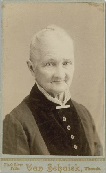 Quarter-length portrait of an elderly woman with gray or white hair pulled up in a bun. She is wearing a dress with buttons on the bodice, and a white ruffled collar and collar pin.