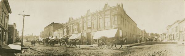 Panoramic view from street of Martin Lein/Lien's funeral procession, showing Main and Water Streets before the flood of 1911. The procession includes several horse-drawn carriages and some people on foot.
