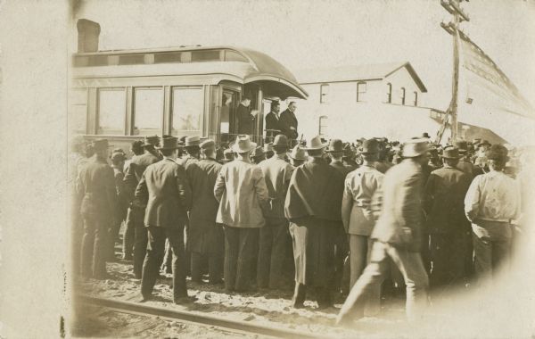 Crowd at railroad station listening to a whistle-stop speaker standing on the back of a caboose. Probably William McKinley.