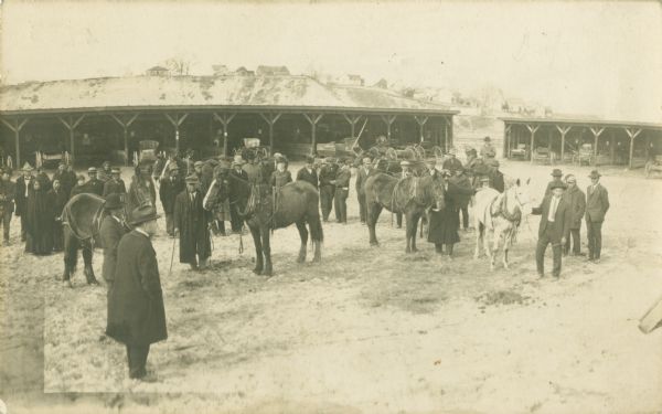 Elevated view of group of people and horses in front of horse sheds for farmers after the 1911 flood, looking north, downtown on Harrison Street. In the far background are houses on a hill.