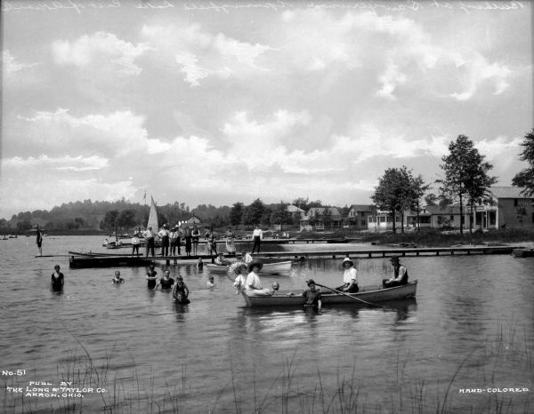 Boaters, swimmers, and people standing on a dock pose for a portrait on Springfield Lake. Several houses and trees stand along the shore in the background.