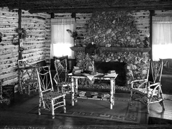 View of the dining room in White Birch Lodge.  The view features a stone fireplace and a table and chairs made of birch logs.