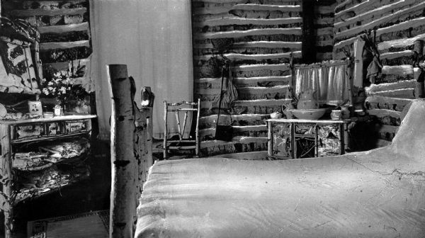 View of a bedroom at White Birch Lodge. The room is furnished with a bed, dressing table, and chair made out of birch logs.