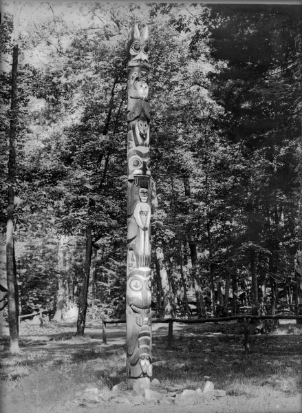 A totem pole stands in front of trees and a wooden fence at Camp Lenape.