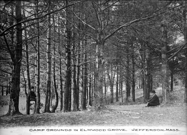 Two men wearing hats and suit coats sit in a wooded area at the Elmwood Grove campgrounds.