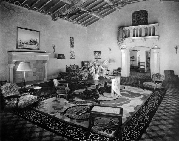 View of the lounge of the Westward-Ho Hotel. The room features a decorative arch doorway on the right, a fireplace, patterned flooring, furniture, and artwork on the walls.
