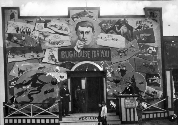 Entrance to Bug House Amusement Park (?).  View features several people standing in front of the entrance to the building, which features elaborate painting and decorations. The lettering on the building reads "Bug House For You".