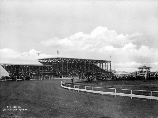 View of the State Fair Grounds featuring a race track and a crowd seated in the grandstands.