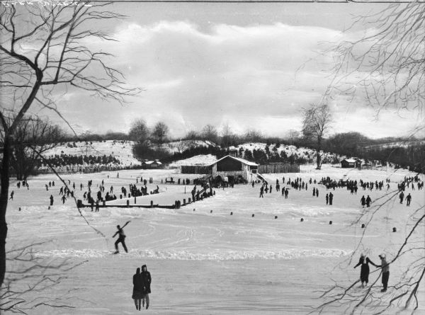 View of people playing winter sports (sking and skating) at Virginia Kendall Park, a large, snow-covered area with a dwelling in the background.