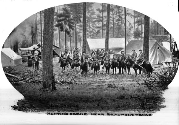 Hunters on horseback prepare for a hunt in front of a campsite with many trees and tents.