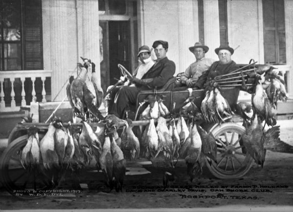 Four hunters sit in an automobile parked in front of the Oak Shore Club and laden with dead ducks and geese after hunting.