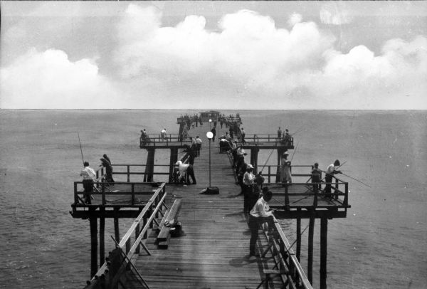 People fish from a wooden pier.