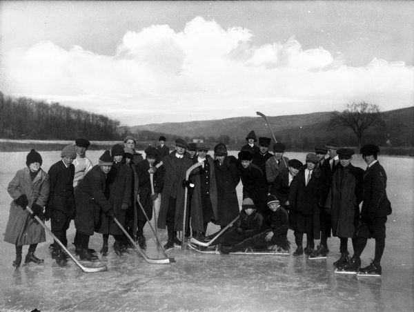 A group of boys from Eymard Seminary wearing ice skates and winter dress while holding hockey sticks.