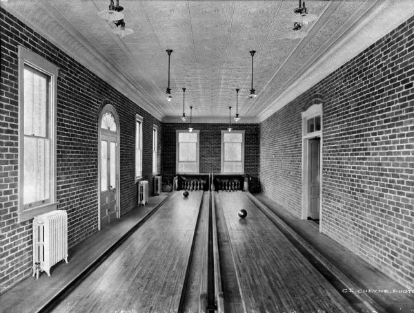 View of a two-lane bowling alley surrounded by brick walls and windows at Old-Point-Comfort College.