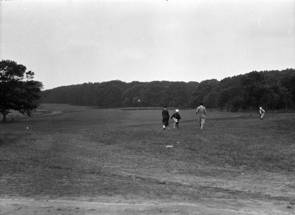 Several golfers and caddies walk along the fairway of Shelter Island Height golf course.