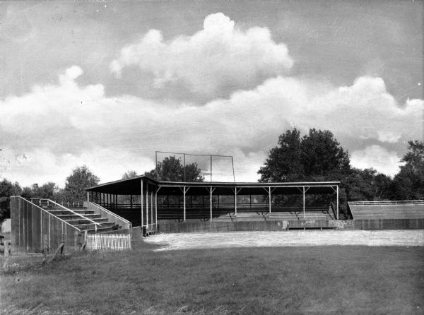 A pavilion, bleachers, a fence, and trees in the background of a ballpark.