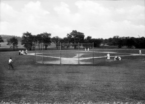 Uniformed boys play baseball at Brunnerdale Seminary. A fence and trees stand in the background.