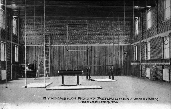 View of the Perkiomen Seminary Gymnasium featuring brick walls, climbing ropes, rings, and gymnastics equipment.