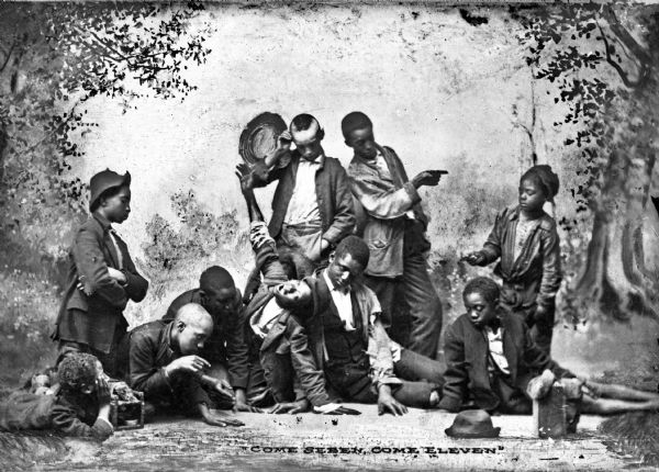 African-American boys gather for a "studio group photo in the condescending idiom of about 1900." The boys stand in a wooded area while imitating a game of "shooting craps."