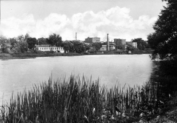 View of the Rock River featuring a shoreline across the river with several buildings (possibly industrial plants), two towers, and many trees.