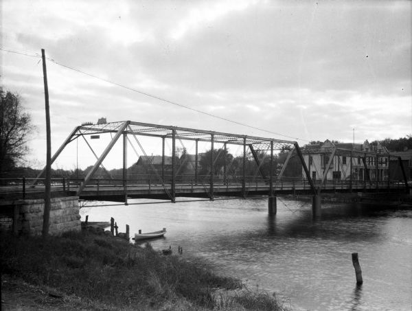 View of a bridge with a boat passing beneath it.  Several dwellings are visible in the background.