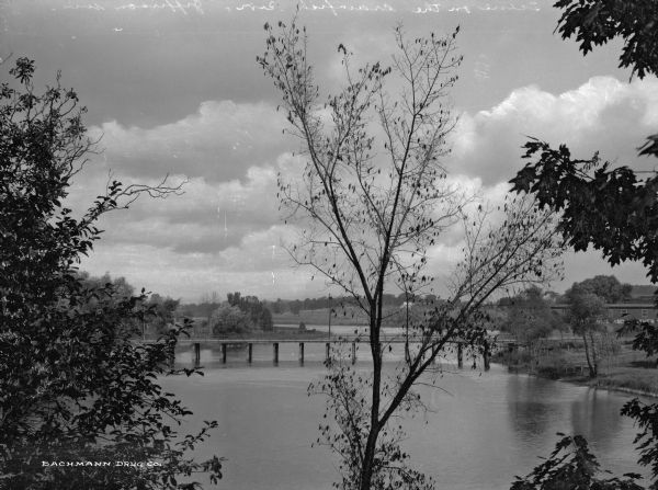 A bridge crosses the Crawfish River.  A dwelling stands along the tree-covered shoreline.