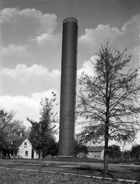 A standpipe water tower stands between what appears to be a farmhouse and a barn.