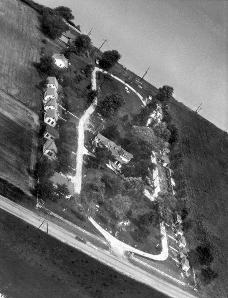 Aerial view of the Villa St. Joseph featuring the main house in the center of the image, surrounded by a road and many smaller dwellings. A road runs in front of the complex, and trees are scattered throughout.