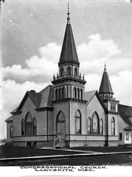 Exterior view of the Congregational Church.  The building features two decorative steeples, arched windows, and stairs leading up to the entrance of the church.