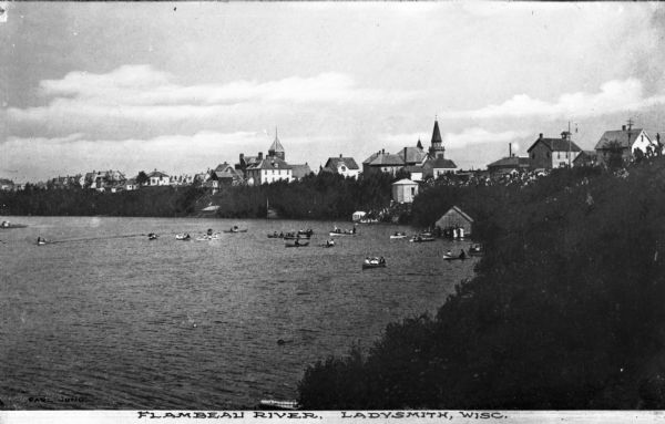 Elevated view of the Flambeau River including boats on the river and buildings (possibly resorts) standing along the forested shore.