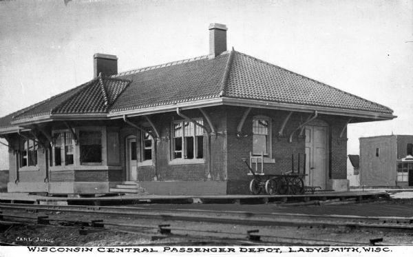 Exterior view of the Wisconsin Central Passenger Depot.  The brick building is surrounded by a wooden platform and railroad tracks run through the foreground.