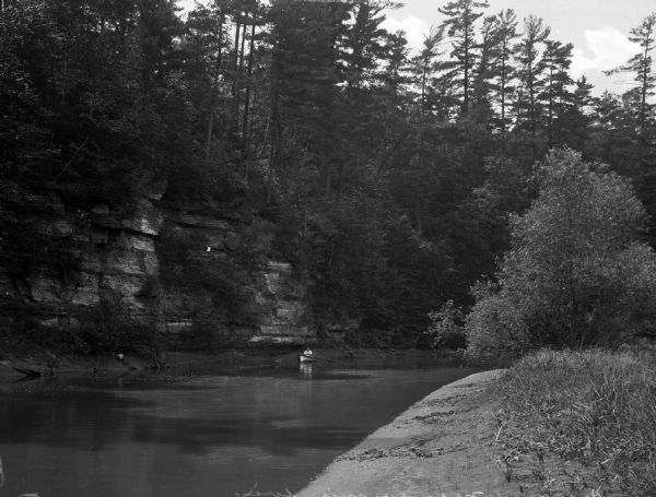 A person rows a boat through Wilson's Creek.  Rock formations and trees stand on the shores.
