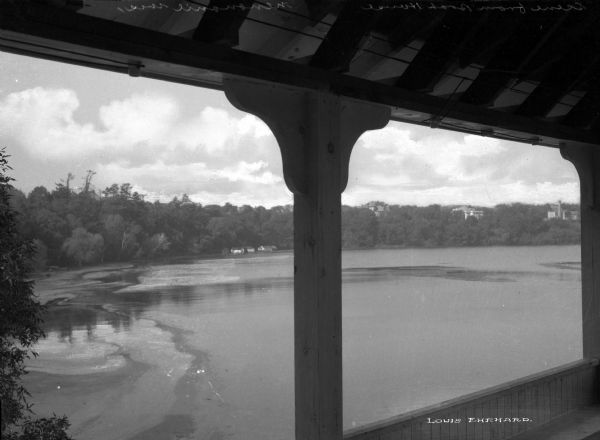 View of a lake, several dwellings, and a forested shoreline seen from an elevated boathouse.