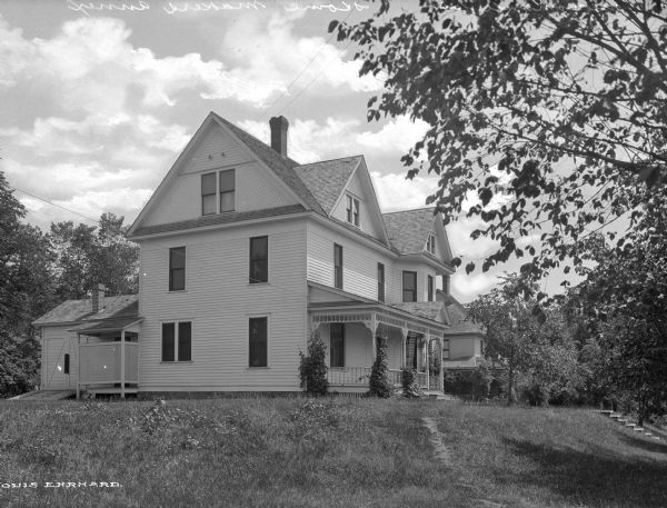 View of the Home Makers Annex, a three-story house with an ivy covered porch, a lawn, and several trees in the background.